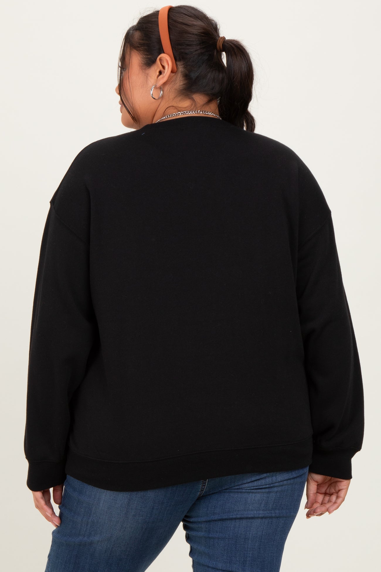 woman wearing a black oversized sweatshirt, viewed from the back, paired with blue jeans