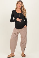 woman wearing a black long sleeve maternity top and beige relaxed-fit pants, holding her baby bump