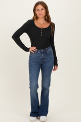 woman wearing a black long sleeve ribbed top with buttons and blue flared jeans standing upright