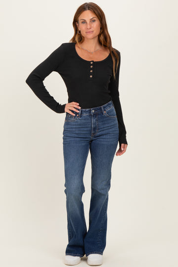 woman wearing a black long sleeve ribbed top with buttons and blue flared jeans standing upright