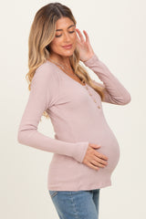 woman wearing a light pink ribbed maternity top with buttons, showing her baby bump while smiling