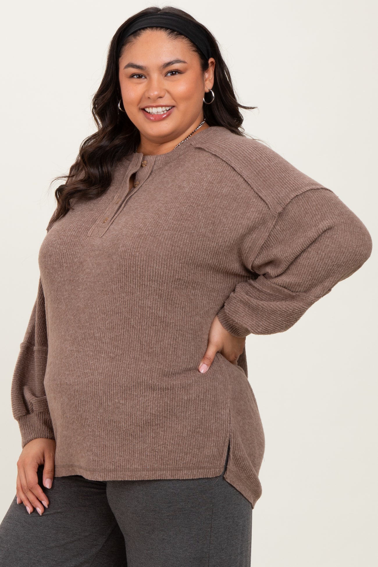 woman wearing a brown plus size ribbed pullover with a henley neckline and oversized fit, smiling at the camera