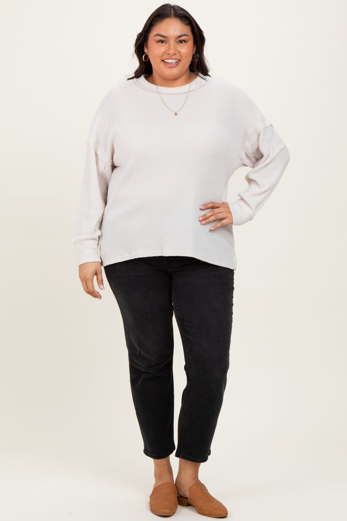 woman wearing a light beige oversized sweater and black slim-fit jeans, posing with brown slip-on shoes