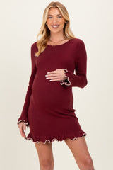 woman wearing a burgundy long sleeve maternity dress with ruffle hem and accent trim, holding her baby bump