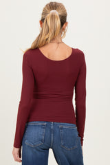 woman wearing a maroon long sleeve maternity top viewed from the back with fitted design and curved hem