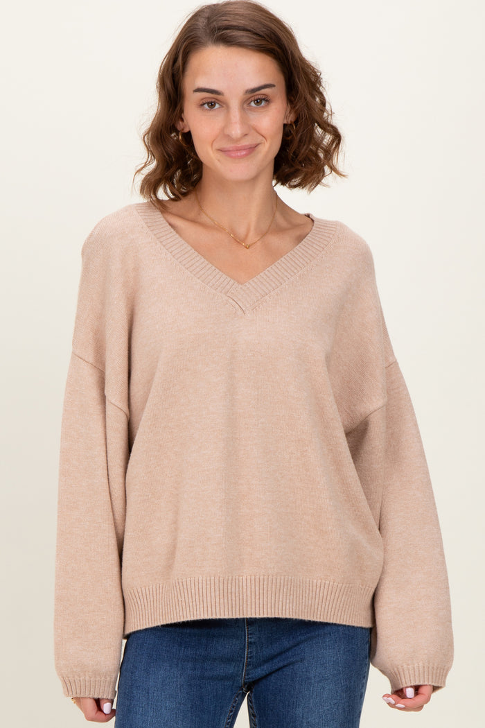 woman wearing a beige oversized v-neck sweater with long sleeves and relaxed fit, paired with blue jeans