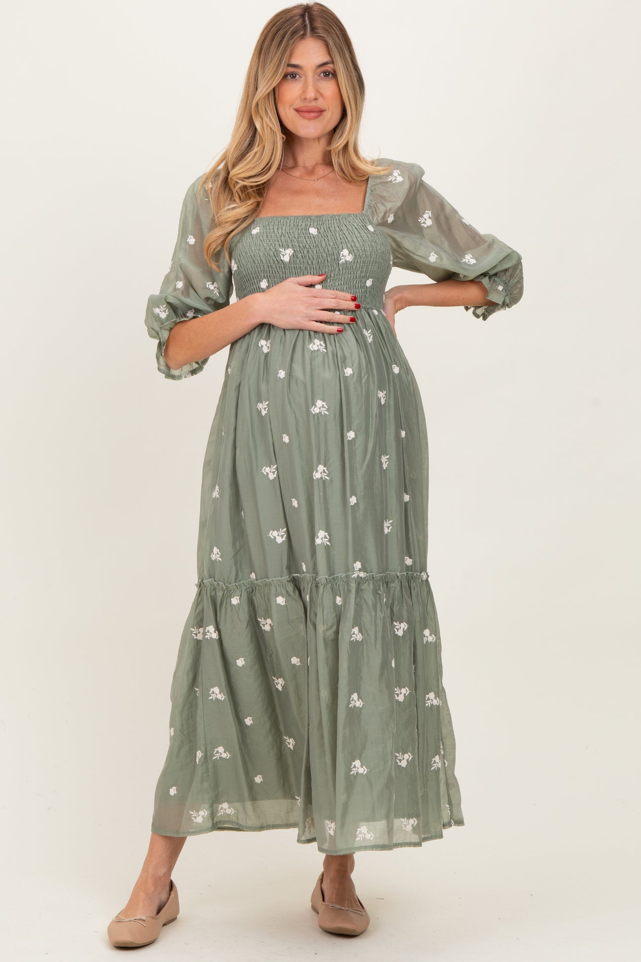 woman wearing a green floral embroidered maternity dress and holding her baby bump