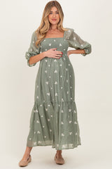 woman wearing a green floral embroidered maternity dress and holding her baby bump