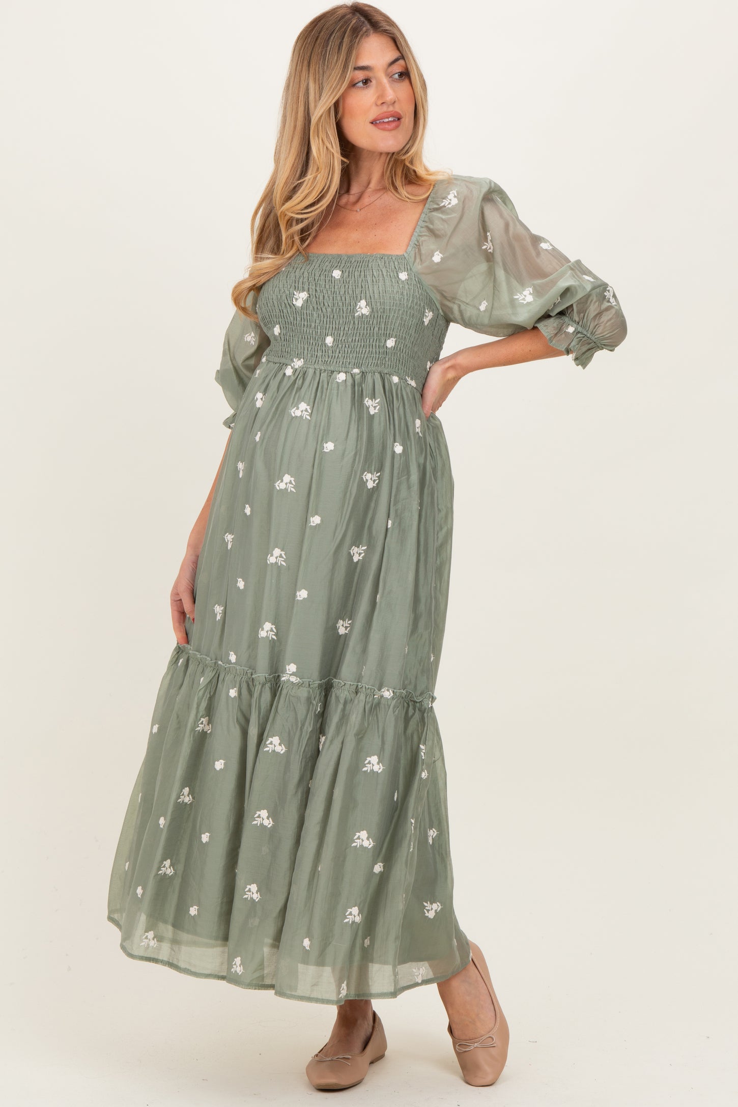 woman wearing a green maternity maxi dress with floral embroidery and puff sleeves, showcasing a baby bump