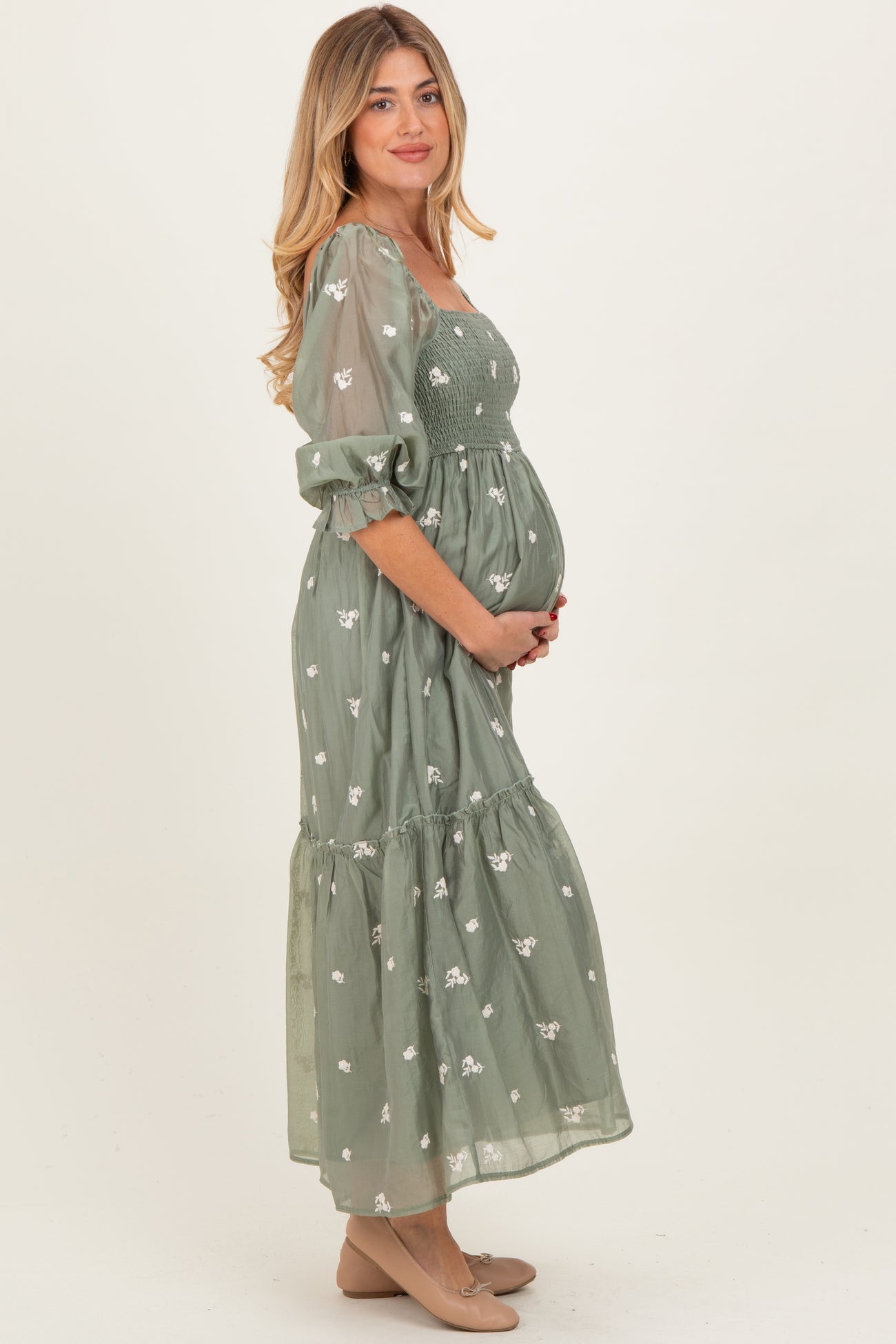 woman wearing a green floral maternity maxi dress with puff sleeves and holding her baby bump