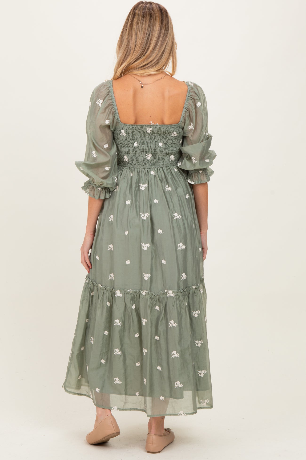 woman wearing a green embroidered maternity dress with puff sleeves and a long skirt, showcasing a baby bump from the back