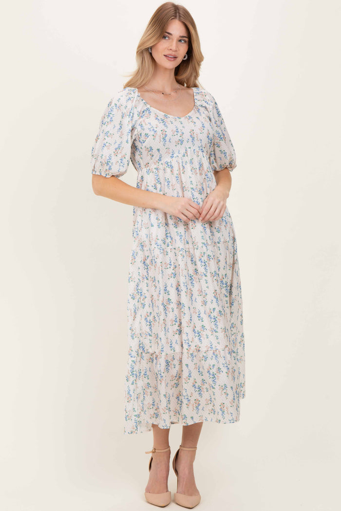 woman wearing a floral-printed maxi dress with puff sleeves and a square neckline, standing in neutral heels