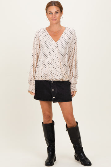 woman wearing a cream polka dot wrap blouse with long sleeves and a black denim button skirt, paired with knee-high black boots