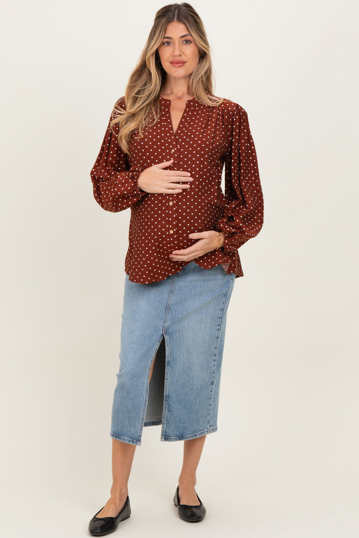 woman wearing a burgundy polka dot maternity top and a denim skirt, gently holding her baby bump