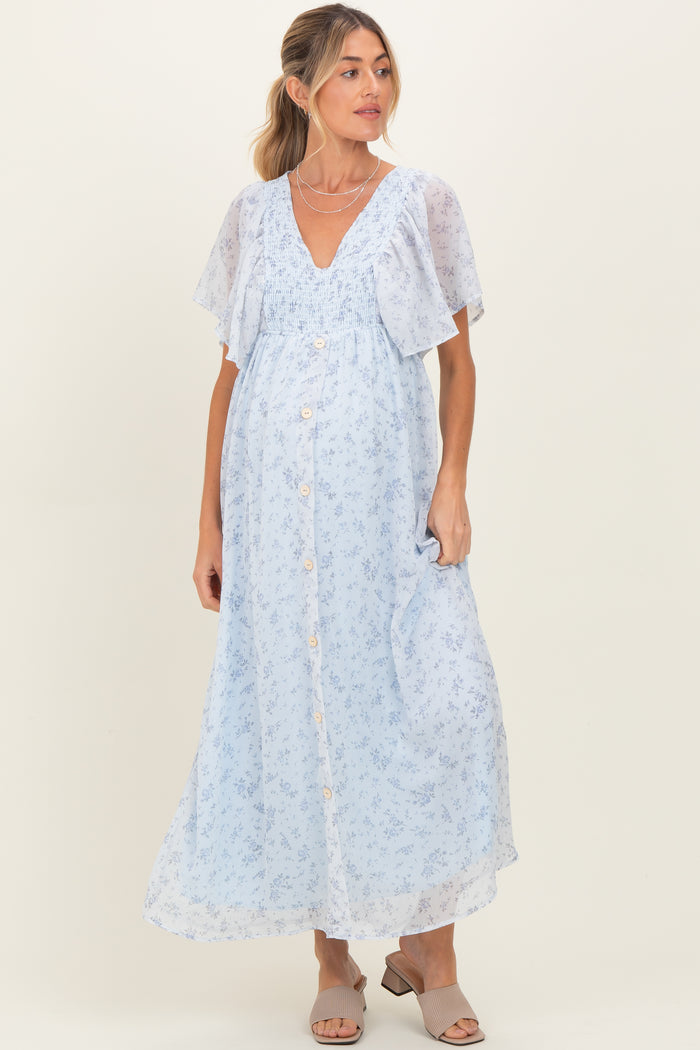 woman wearing a light blue floral print maxi maternity dress with short flutter sleeves and button details, showing her baby bump
