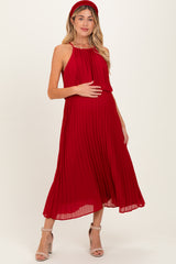 woman wearing a red pleated maternity dress and holding her baby bump
