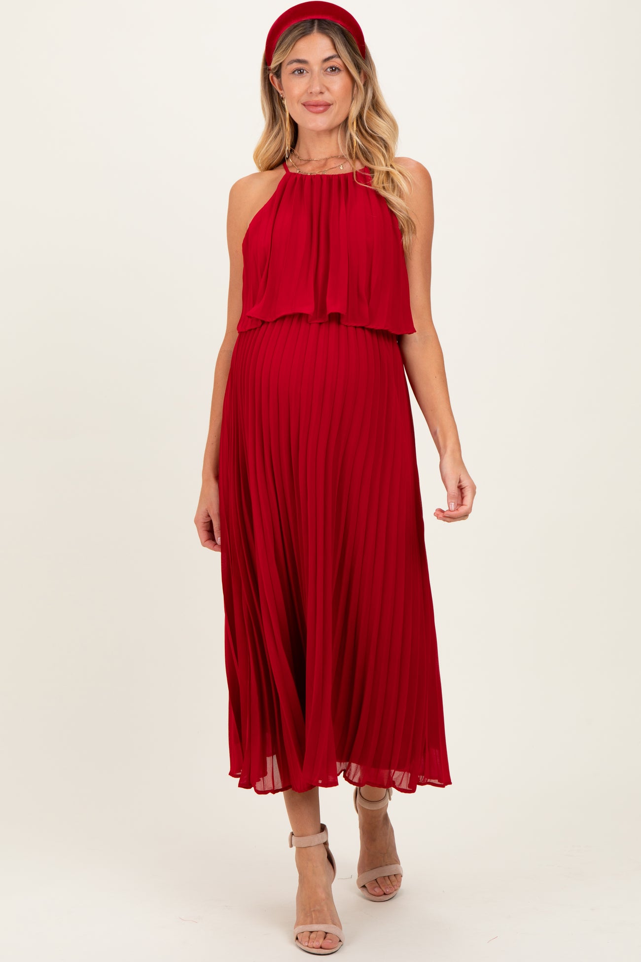 woman wearing a red pleated maternity dress with a halter neckline and flowing skirt, showcasing her baby bump