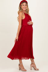 woman wearing a red pleated maternity dress, showing off her baby bump, paired with a matching headband and heels