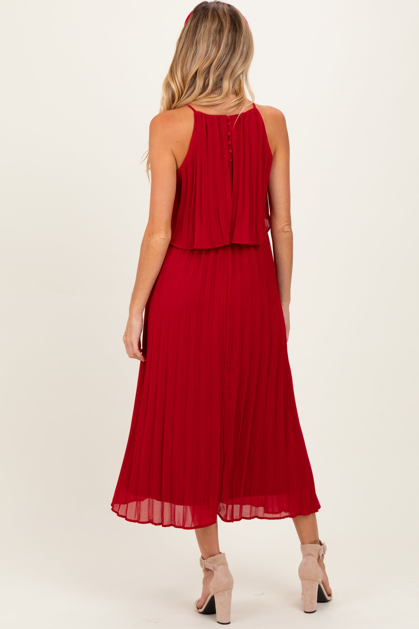 woman wearing a red pleated maternity dress with a keyhole back and layered top, showing a baby bump