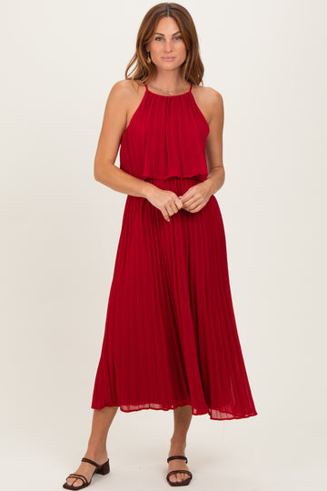 woman wearing a red pleated midi dress with a halter neckline and layered bodice, standing in a neutral background