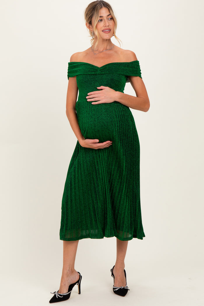 woman wearing a green off-the-shoulder maternity dress with a pleated skirt and holding her baby bump