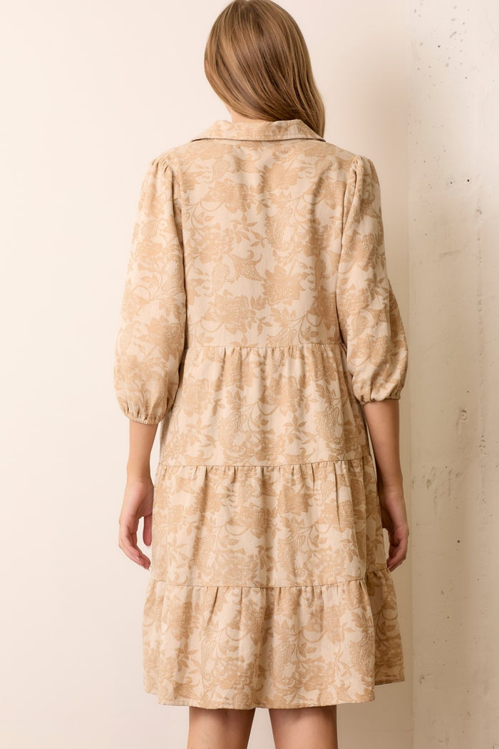 woman wearing a beige floral printed tiered dress with long puff sleeves and a collar, shown from the back