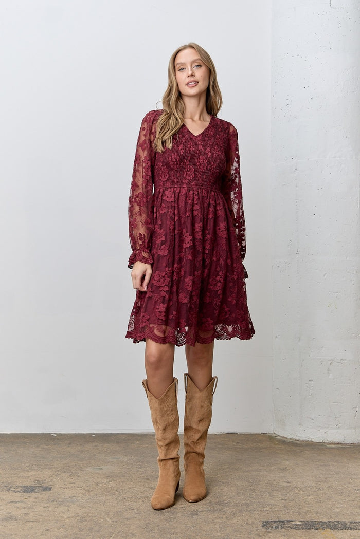 woman wearing a burgundy long sleeve lace dress with a smocked bodice and ruffled hem, paired with tan suede boots