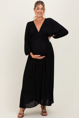 woman wearing a black maxi maternity dress with a deep v-neck and gathered bodice, holding her baby bump