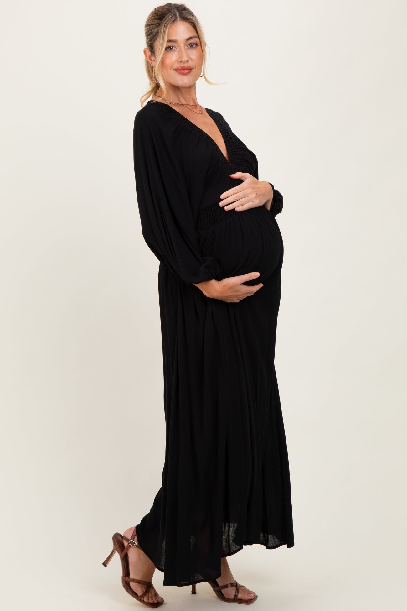 woman wearing a black maxi maternity dress with a deep v-neck and long sleeves, holding her baby bump