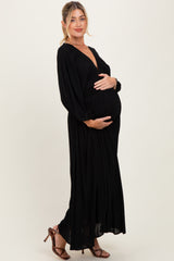 woman wearing a black maxi maternity dress with a deep v-neck and long sleeves, holding her baby bump