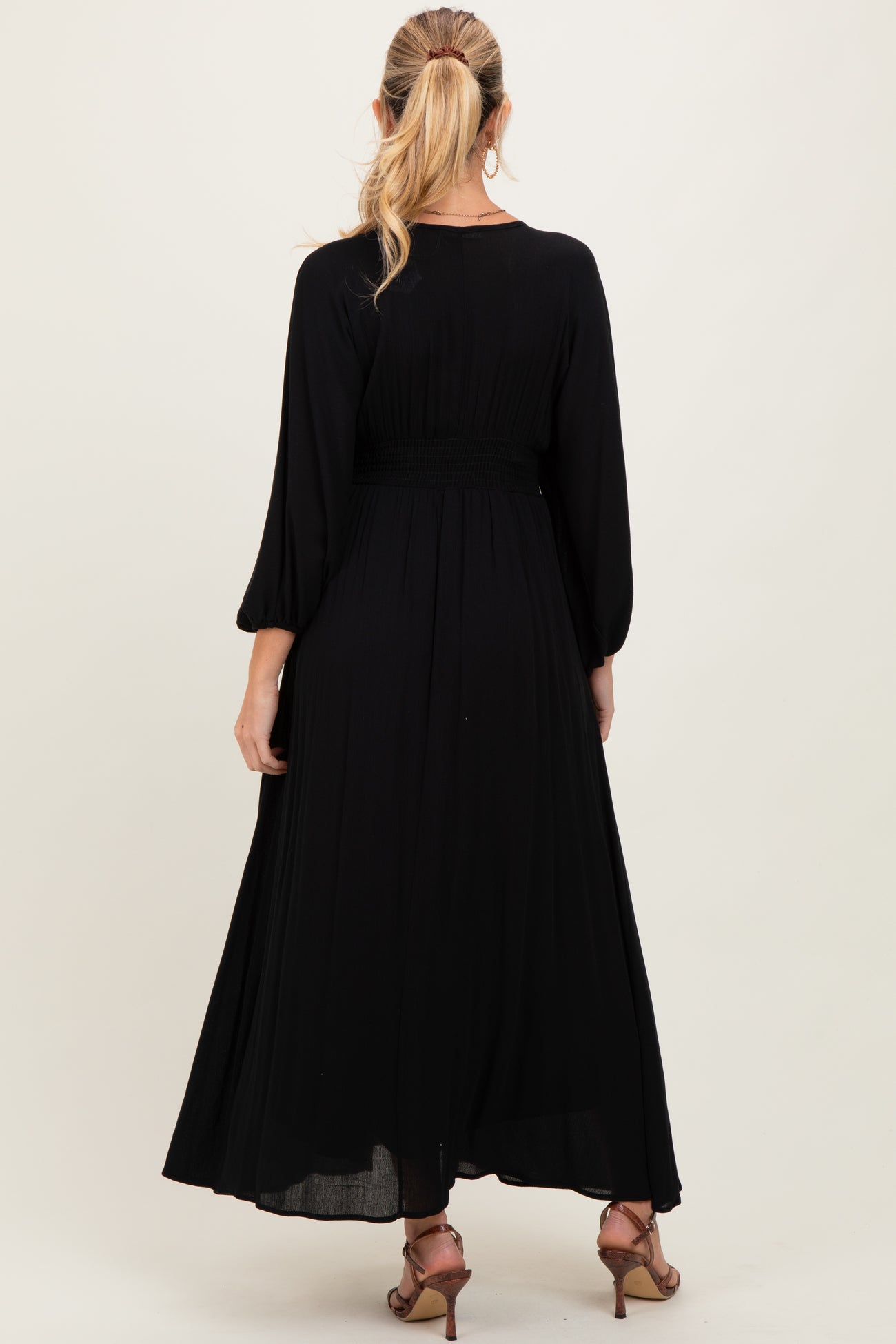 woman wearing a black maternity maxi dress with long sleeves and smocked waistband, facing away from the camera