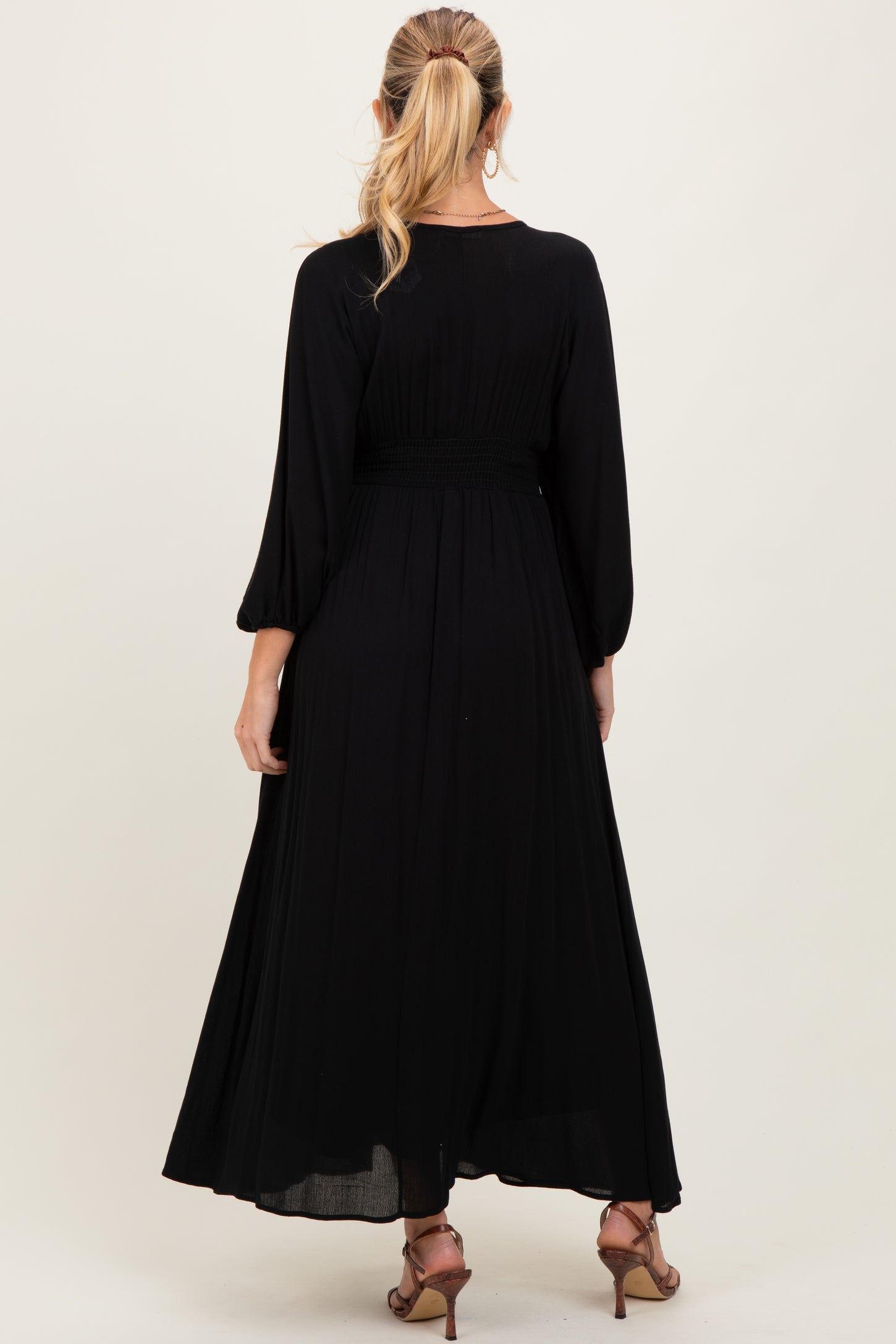 woman wearing a black maternity maxi dress with long sleeves and smocked waistband, facing away from the camera