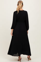 woman wearing a black maternity maxi dress with long sleeves and smocked waistband, facing away from the camera