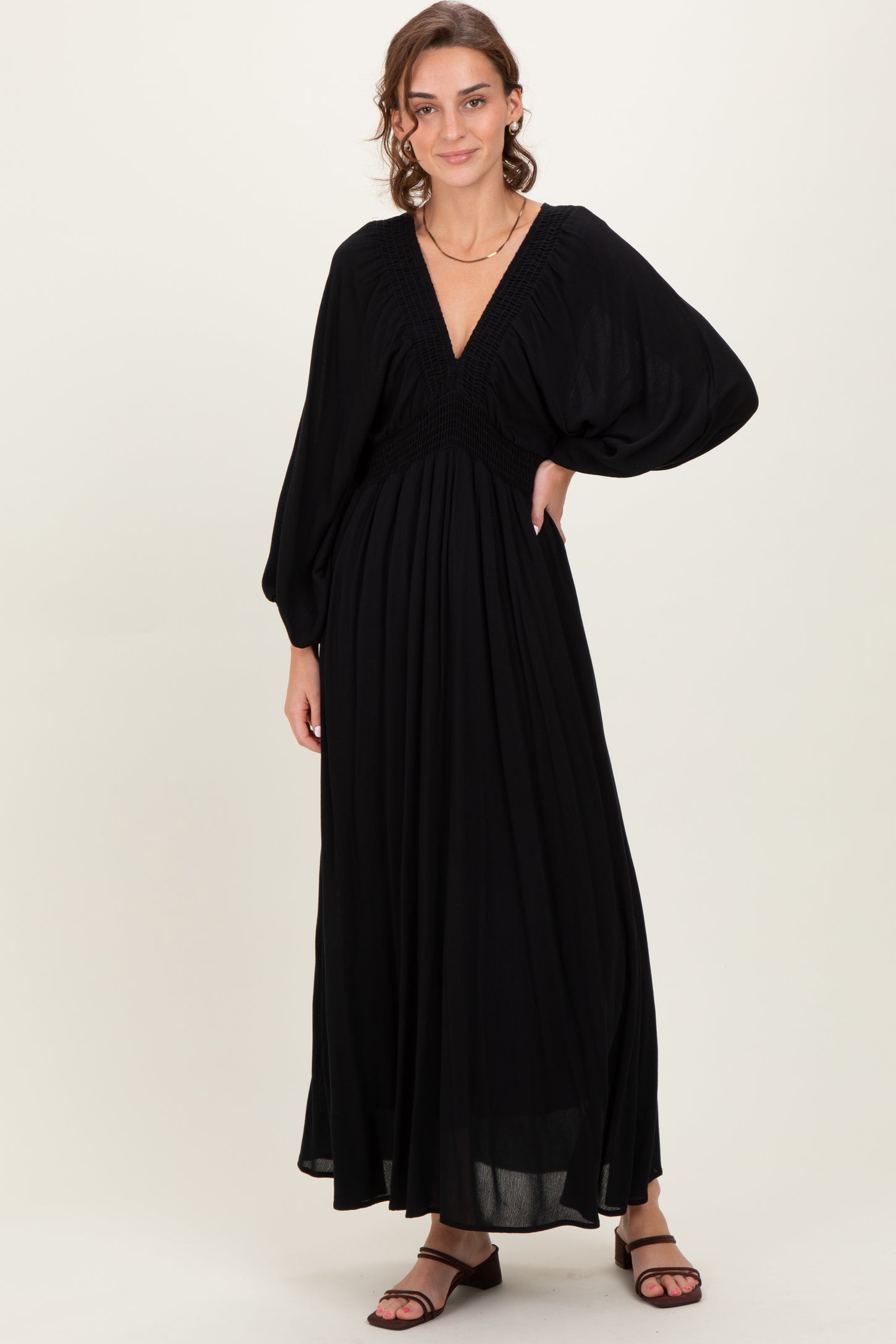 woman wearing a black long sleeve maxi dress with a deep v-neck and smocked bodice, standing in a neutral background