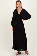 woman wearing a black long sleeve maxi dress with a deep v-neck and smocked bodice, standing in a neutral background
