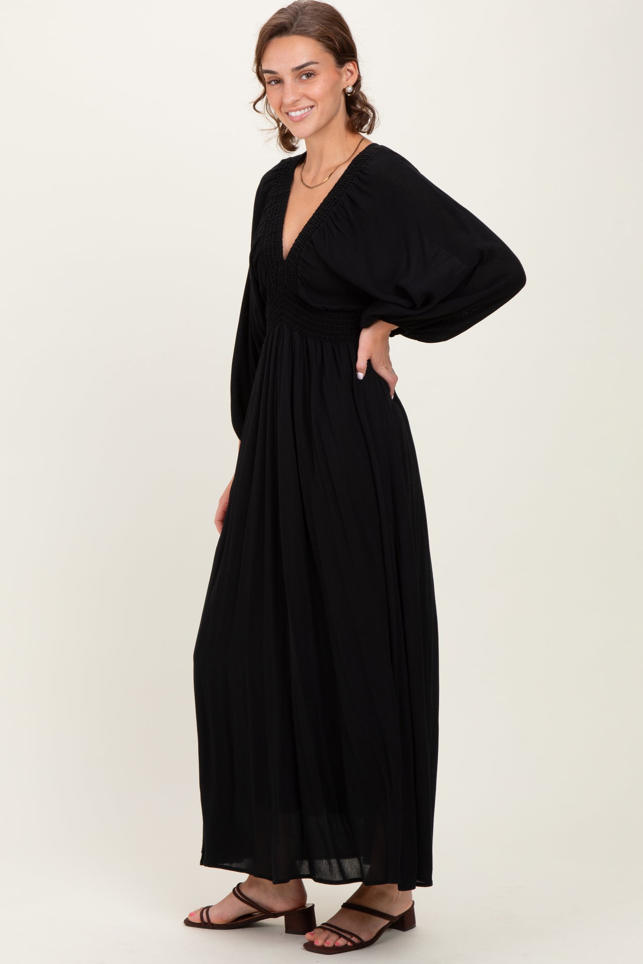 woman wearing a black maxi dress with a deep v-neck and puff sleeves, standing sideways with a flowing skirt
