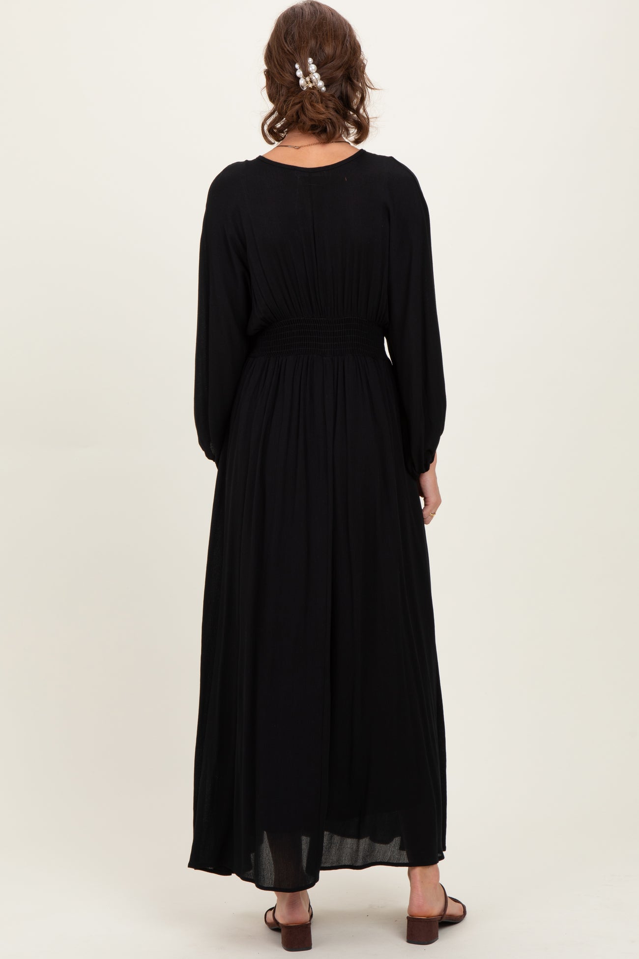 woman wearing a black long sleeve maxi dress with a smocked waistband, shown from the back