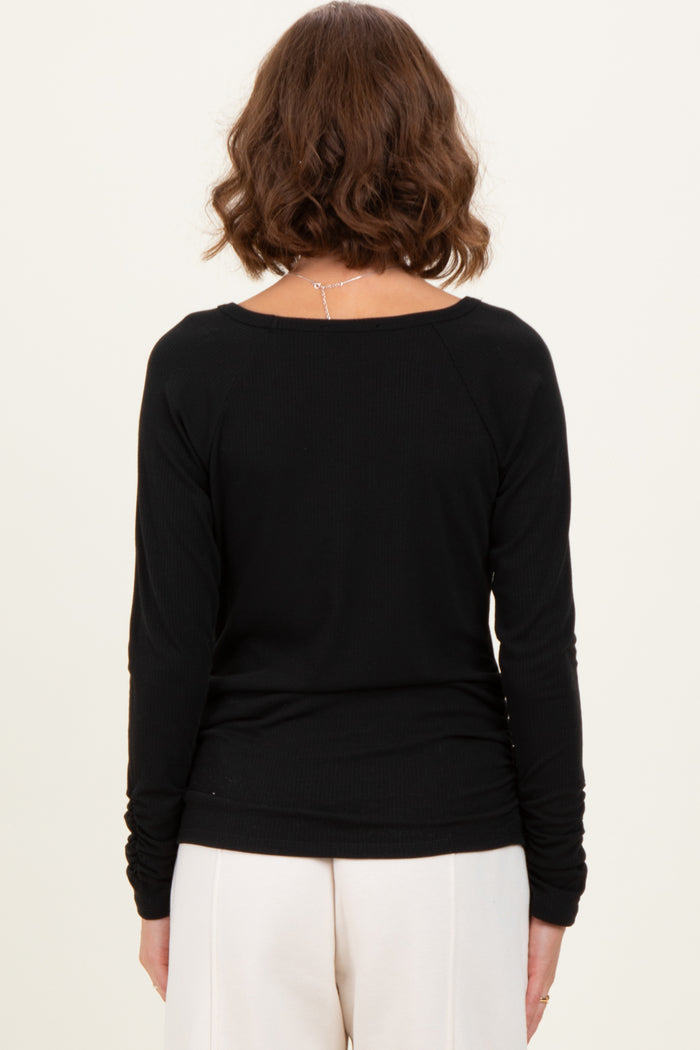 woman wearing a black long sleeve ribbed top, viewed from the back, paired with cream-colored pants