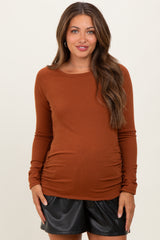 woman wearing a rust long sleeve maternity top with side ruching and black faux leather shorts, showing her baby bump