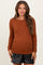 woman wearing a rust long sleeve maternity top with side ruching and black faux leather shorts, showing her baby bump