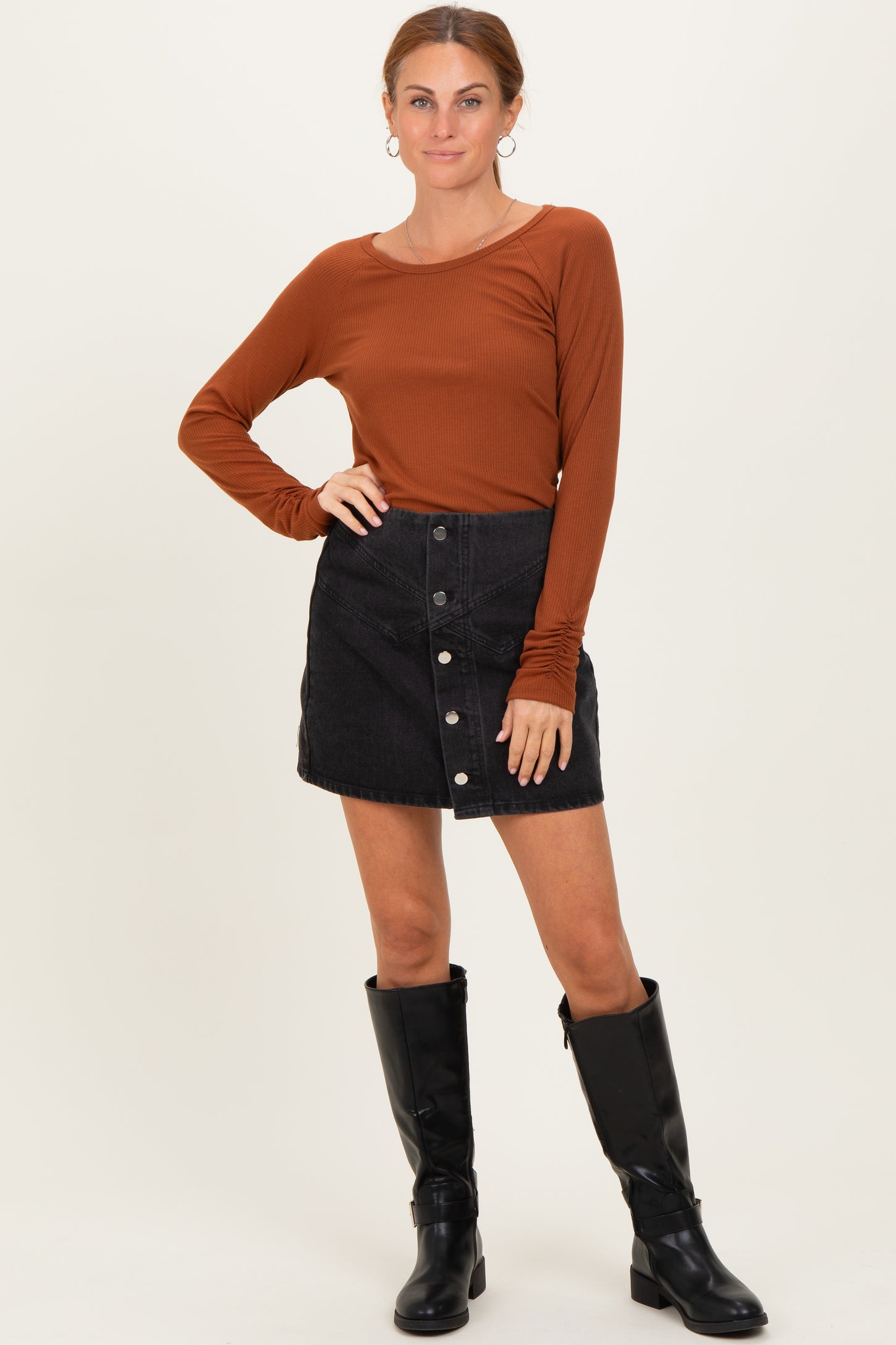 woman wearing a rust long sleeve ribbed top with a black denim button-up mini skirt and knee-high black boots