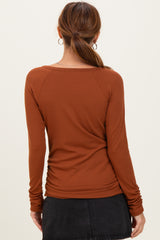 woman wearing a rust long sleeve ribbed top with a round neckline and gathered side details, viewed from the back