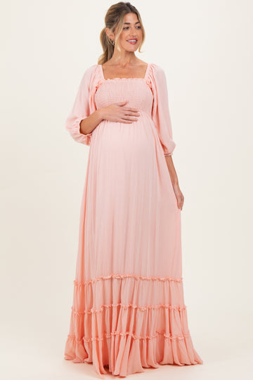 woman wearing a light peach maternity maxi dress with smocked bodice and tiered ruffle hem, holding her baby bump