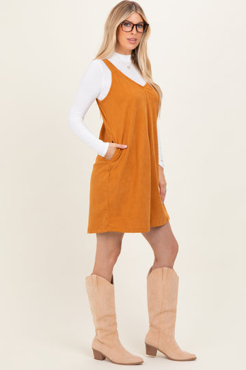 woman wearing an amber suede sleeveless dress with pockets and a white long sleeve top, paired with beige knee-high boots