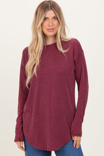 woman wearing a burgundy long sleeve ribbed top with a curved hem and relaxed fit