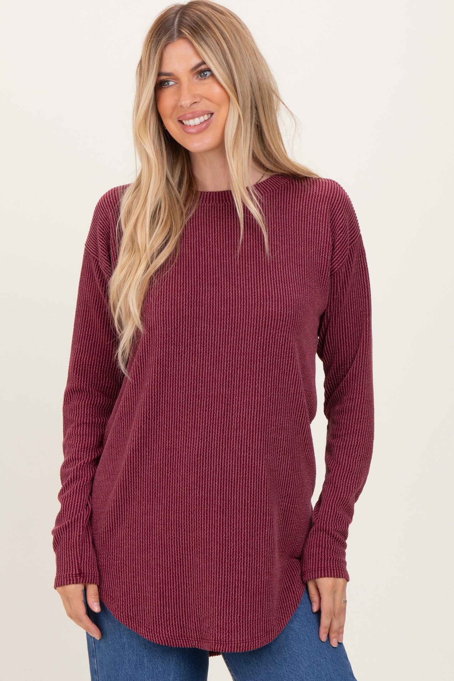 woman wearing a burgundy long sleeve ribbed top with a rounded hem and relaxed fit