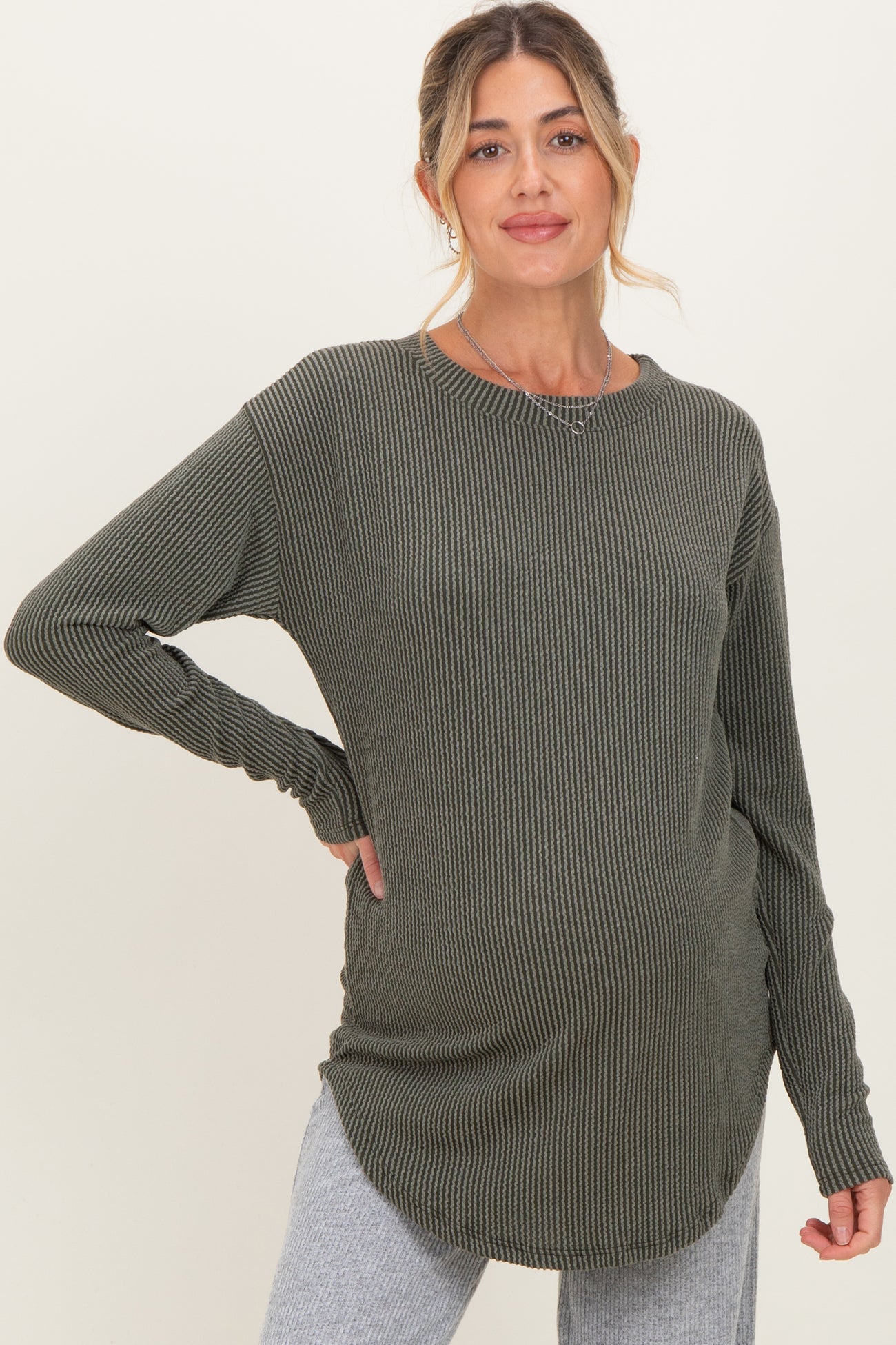 woman wearing a dark green long sleeve maternity top with a ribbed texture and a visible baby bump