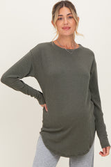 woman wearing a dark green long sleeve maternity top with a ribbed texture and a visible baby bump