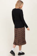 woman wearing a black long sleeve ribbed top and a brown plaid pleated skirt, viewed from the back