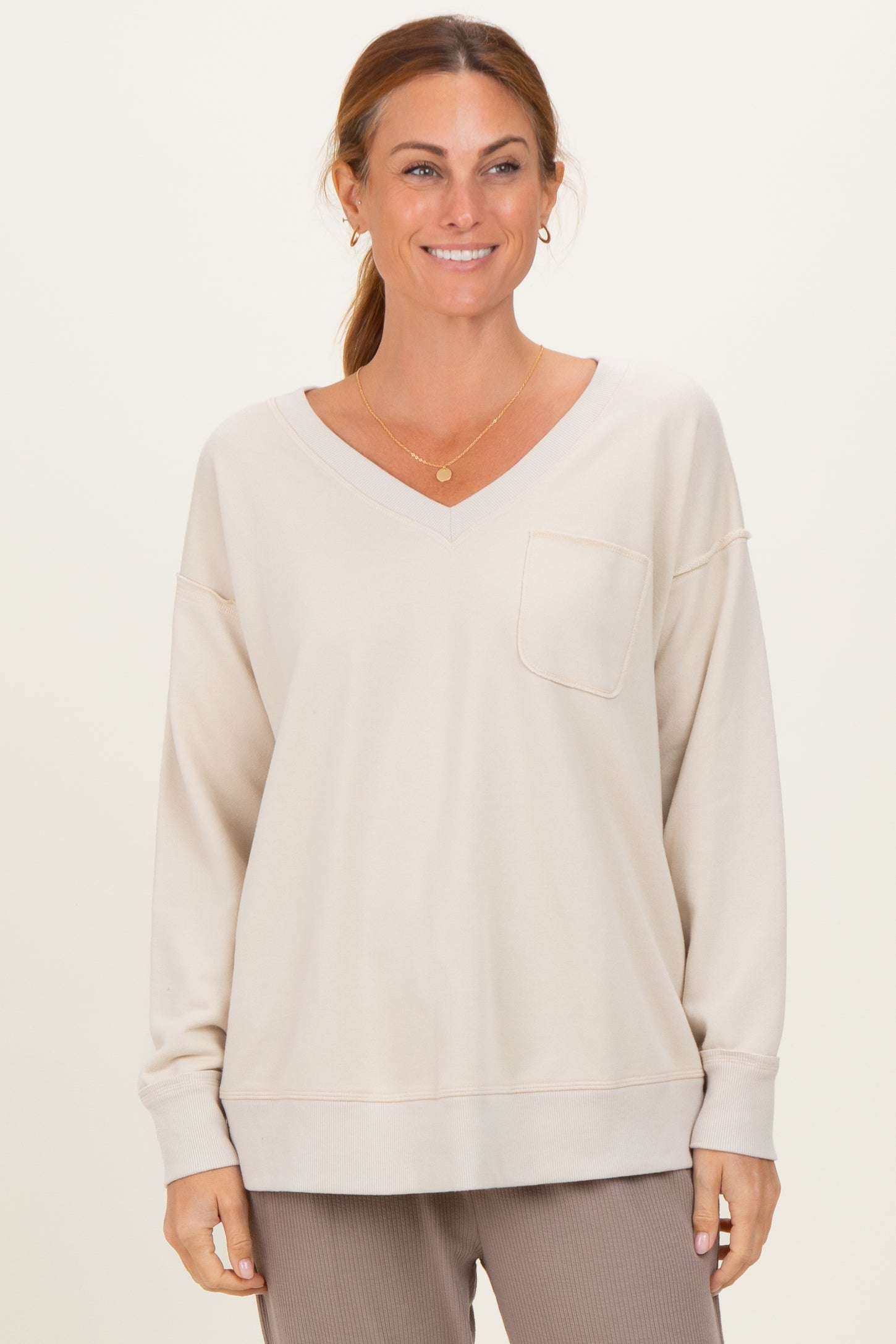 woman wearing a light beige oversized v-neck sweatshirt with a front pocket and relaxed fit
